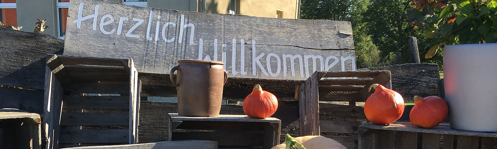 Rustikaler Aufsteller mit der Aufschrift Willkommen - kleine orange Kürbisse, ein Topf aus Ton, Erntekisten - rustikale herbstliche Gestaltung