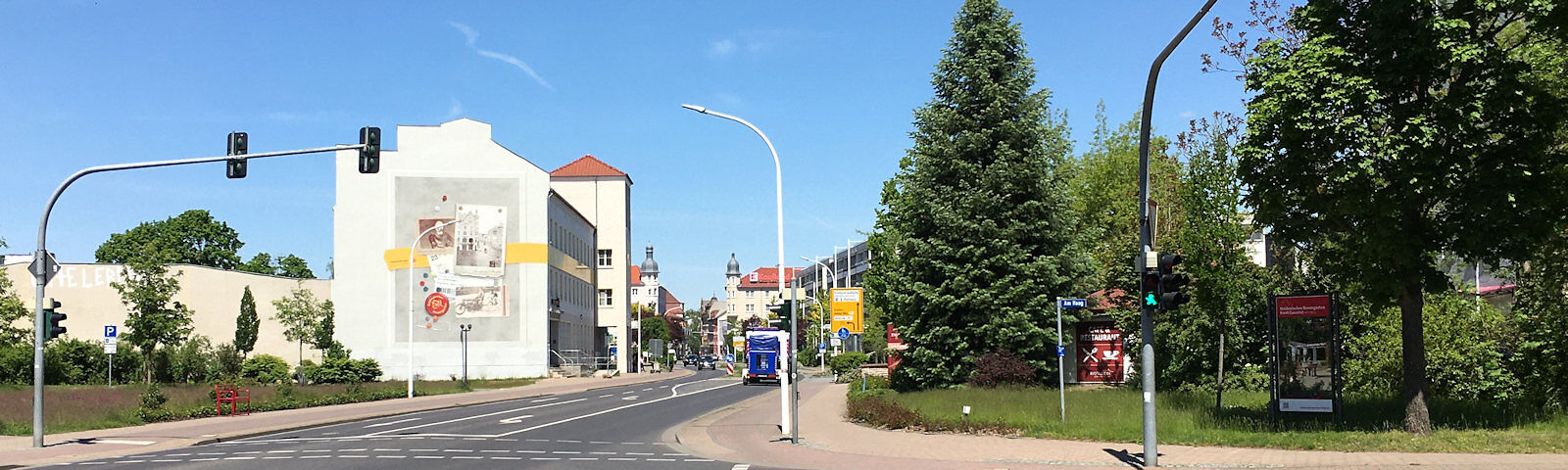 Zu sehen ist die Berliner Straße in Richtung Kaufland, Im Vordergrund eine große Tanne, die Straßenführung mit links- und rechtsseitiger Bebauung.