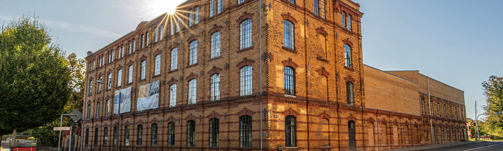 Vor dem Textilmuseum, einem alten Steingebäude, ist vor dem Gehweg ein Bauzaun aufgestellt worden. Das kleinere Nebengebäude hinter dem Museum ist mit einem Gerüst umstellt. Über den Hof des Museums verlaufen zwei Schienen, die in der Mitte des Hofes ineinander übergehen